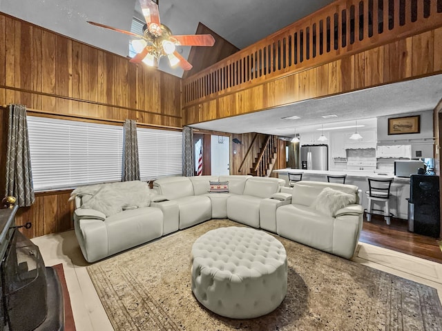 living room with ceiling fan, wood finished floors, wood walls, and stairs