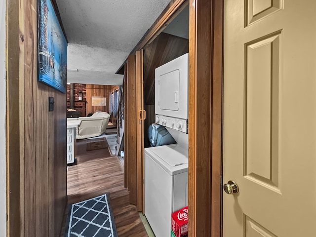 clothes washing area featuring dark wood-style flooring, stacked washer and dryer, wood walls, a textured ceiling, and laundry area