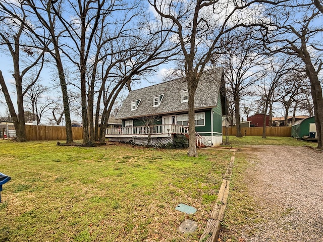 back of house featuring dirt driveway, fence, a yard, roof with shingles, and a wooden deck