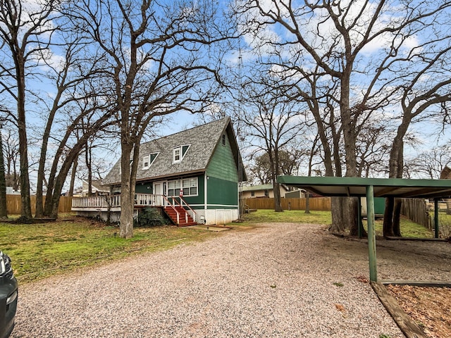 exterior space with a shingled roof, fence, driveway, a wooden deck, and a carport