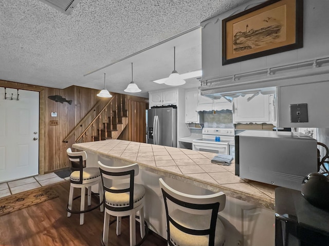 kitchen with stainless steel refrigerator with ice dispenser, a breakfast bar area, tile countertops, white electric range, and wood walls