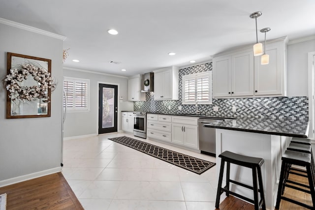 kitchen with ornamental molding, appliances with stainless steel finishes, dark countertops, and wall chimney range hood