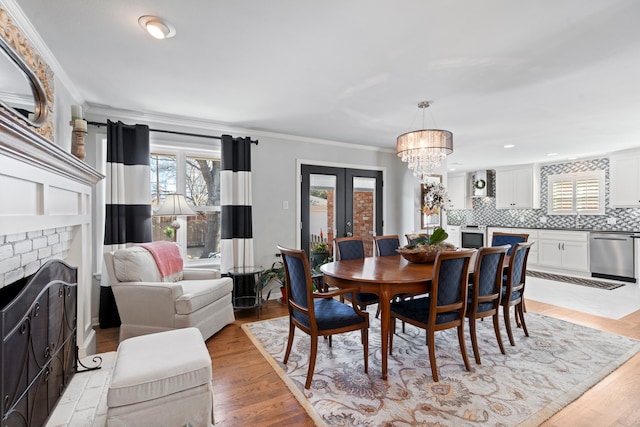 dining room with french doors, crown molding, light wood-style flooring, an inviting chandelier, and a brick fireplace