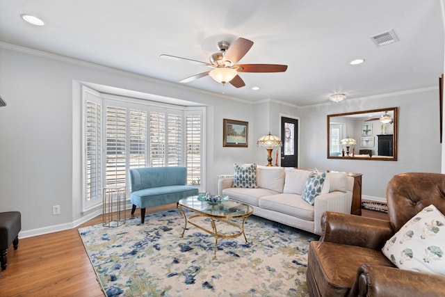 living area featuring visible vents, baseboards, a ceiling fan, wood finished floors, and crown molding