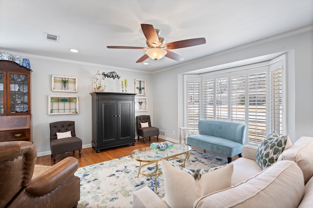 living area featuring a ceiling fan, baseboards, visible vents, light wood-type flooring, and crown molding