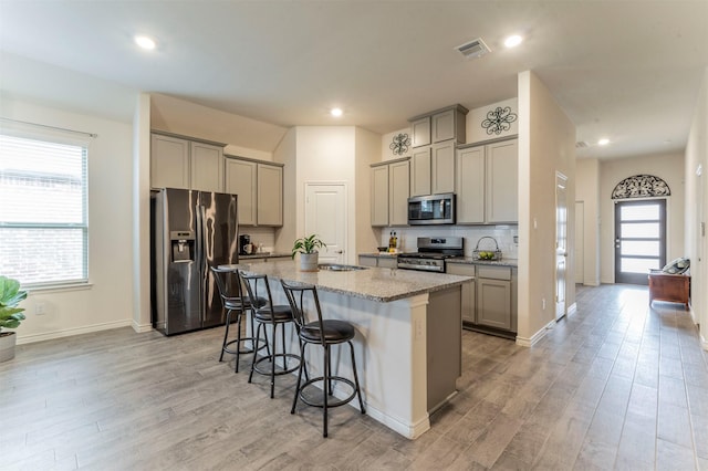 kitchen with a center island with sink, a breakfast bar area, gray cabinets, visible vents, and appliances with stainless steel finishes