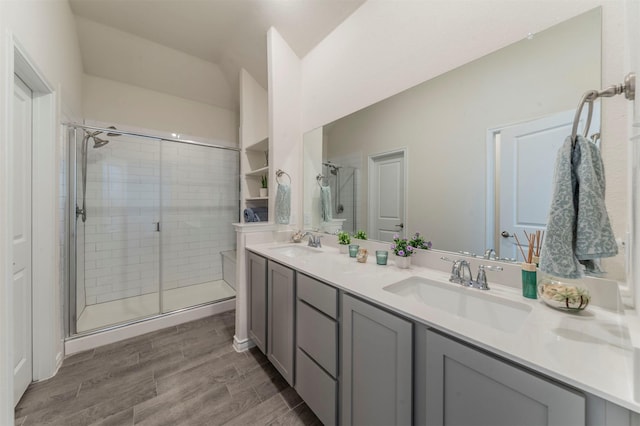 full bathroom with double vanity, a stall shower, a sink, and wood finished floors