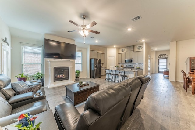 living room with ceiling fan, recessed lighting, visible vents, light wood-style floors, and a glass covered fireplace