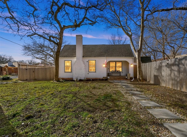 back of property featuring a shingled roof, a chimney, fence private yard, covered porch, and a yard