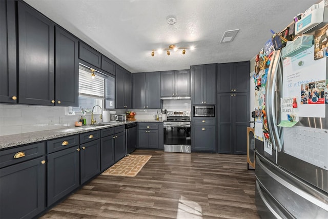 kitchen featuring light stone counters, dark wood finished floors, appliances with stainless steel finishes, a sink, and a textured ceiling