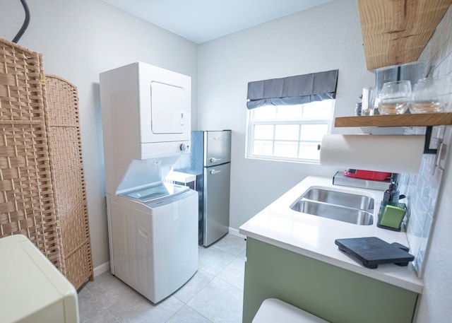 washroom featuring baseboards, light tile patterned flooring, a sink, and stacked washer / drying machine