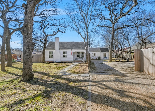 view of front facade with a shingled roof, driveway, a chimney, and fence