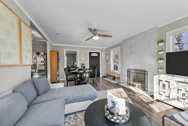 living area featuring crown molding, visible vents, a ceiling fan, a high end fireplace, and wood finished floors