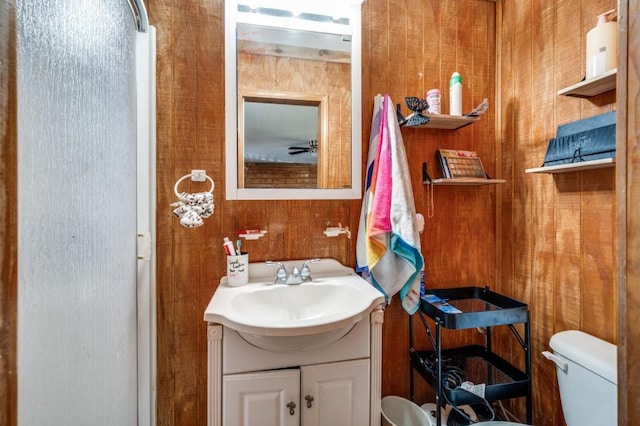 bathroom with wood walls, toilet, and vanity