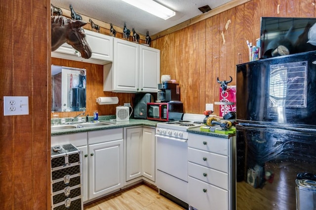 kitchen with white range with gas cooktop, white cabinetry, freestanding refrigerator, light wood-style floors, and wood walls