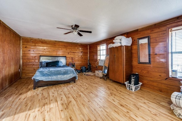 bedroom featuring a ceiling fan, light wood-style floors, and wooden walls