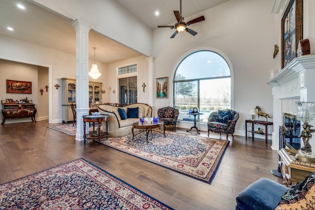 living area with decorative columns, a high ceiling, hardwood / wood-style floors, and a ceiling fan