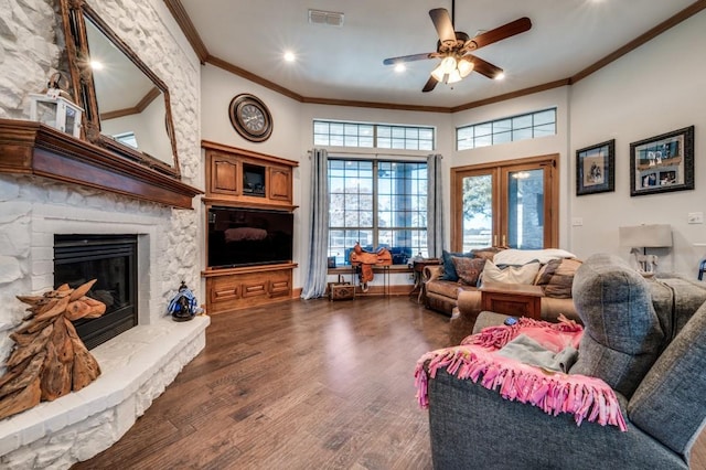 living room with dark wood-style floors, visible vents, a fireplace, ceiling fan, and crown molding