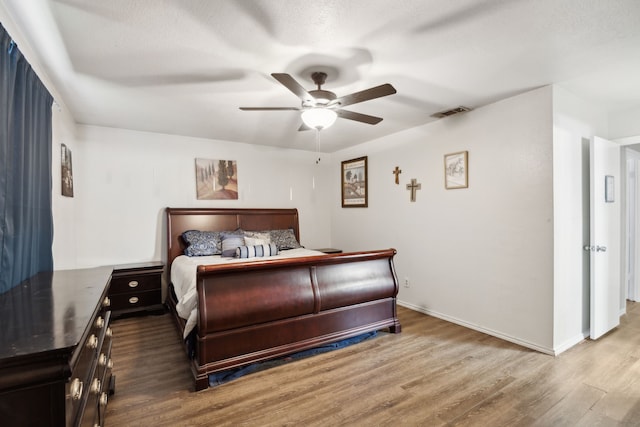 bedroom featuring a ceiling fan, visible vents, baseboards, and wood finished floors