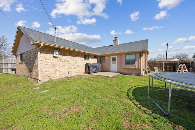 rear view of property featuring a yard, brick siding, a trampoline, and a fenced backyard