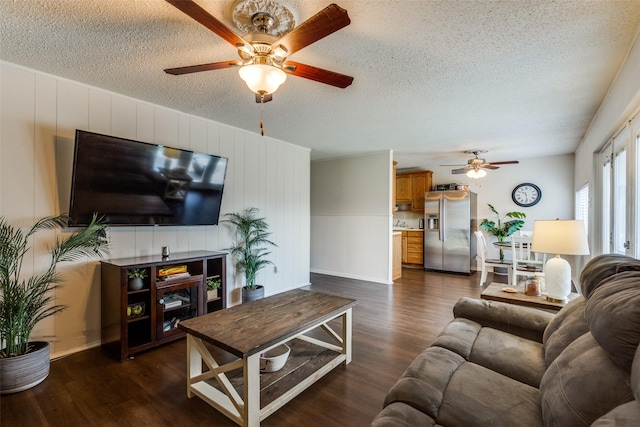 living area with ceiling fan, a textured ceiling, and dark wood-type flooring