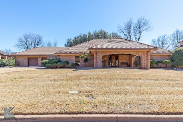 view of front facade with a garage, a front yard, a tile roof, and brick siding