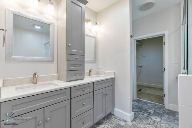 bathroom with double vanity, a sink, a walk in closet, and baseboards