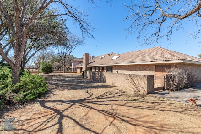 view of side of home featuring a tile roof, brick siding, and fence