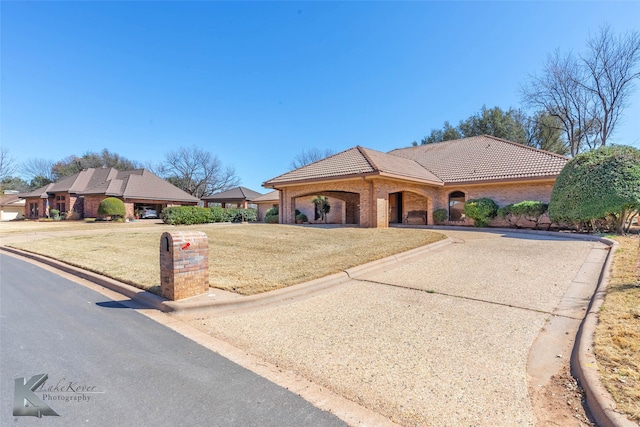 view of front of property featuring a front yard, brick siding, driveway, and a tiled roof