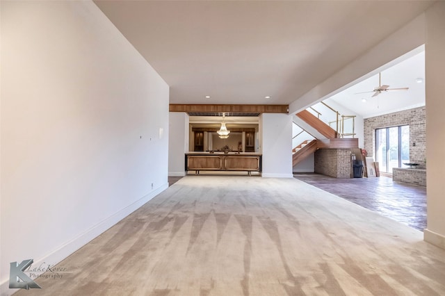 unfurnished living room featuring brick wall, baseboards, stairway, and carpet