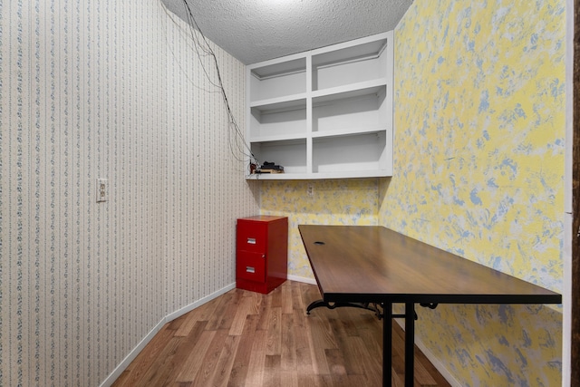 unfurnished office featuring wood finished floors, a textured ceiling, baseboards, and wallpapered walls