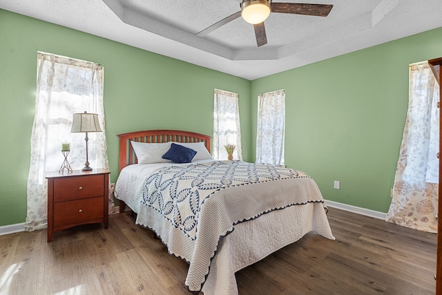 bedroom with a textured ceiling, a tray ceiling, wood finished floors, and baseboards