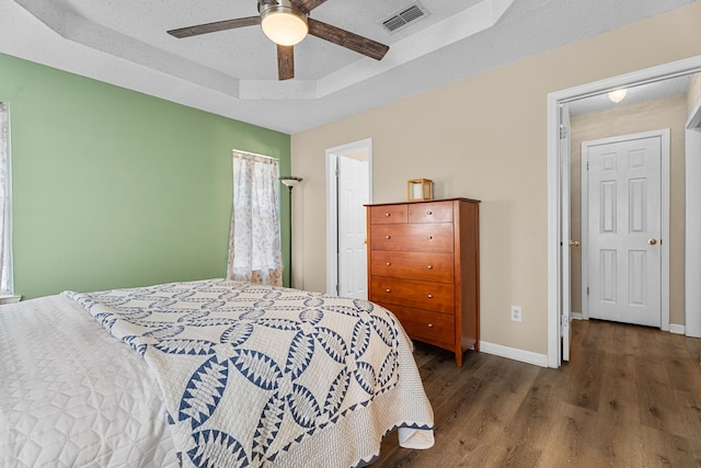 bedroom featuring a tray ceiling, visible vents, a textured ceiling, wood finished floors, and baseboards