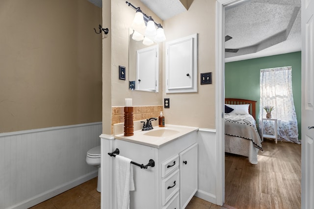 bathroom featuring toilet, ensuite bathroom, wainscoting, a textured ceiling, and vanity