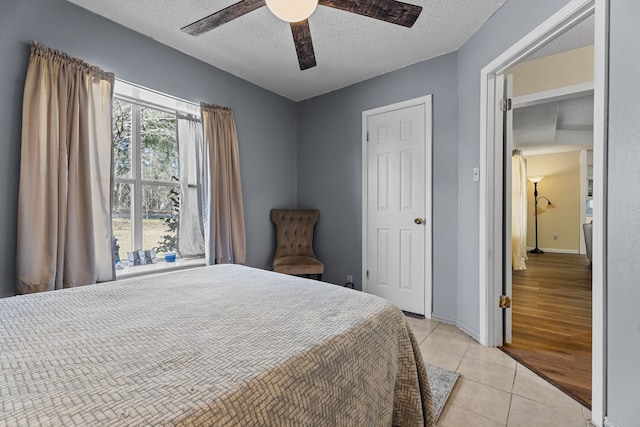 bedroom featuring a textured ceiling, ceiling fan, light tile patterned flooring, and baseboards