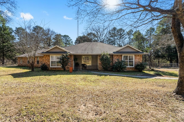 ranch-style home featuring a shingled roof, a front yard, brick siding, and fence