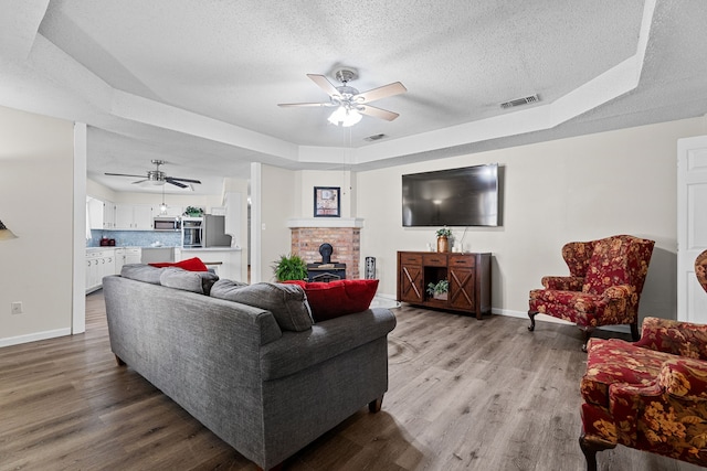 living room featuring a tray ceiling, a wood stove, a textured ceiling, and wood finished floors