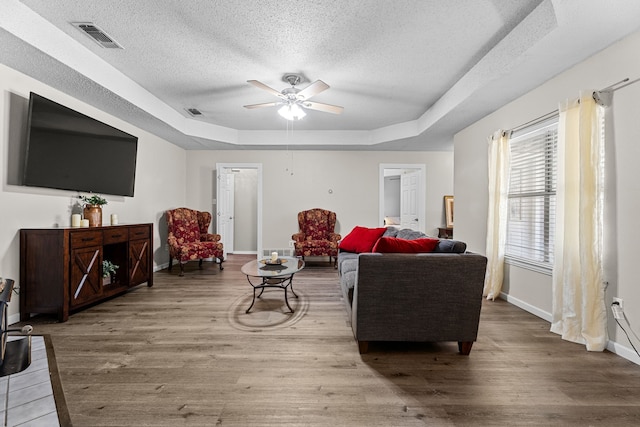 living room with visible vents, a textured ceiling, a tray ceiling, and wood finished floors