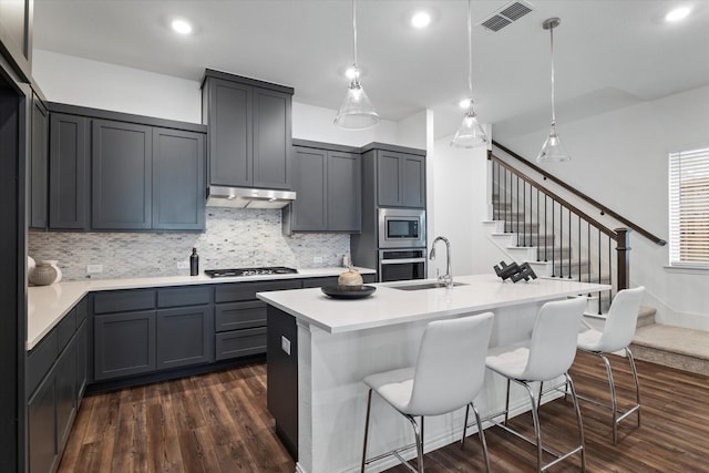 kitchen featuring under cabinet range hood, a sink, visible vents, appliances with stainless steel finishes, and dark wood-style floors