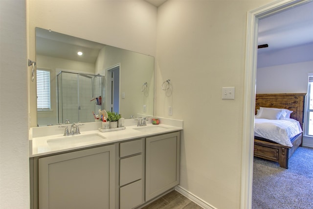 ensuite bathroom featuring a stall shower, a sink, baseboards, and double vanity