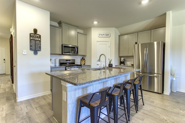 kitchen with stainless steel appliances, gray cabinets, dark stone countertops, and a sink