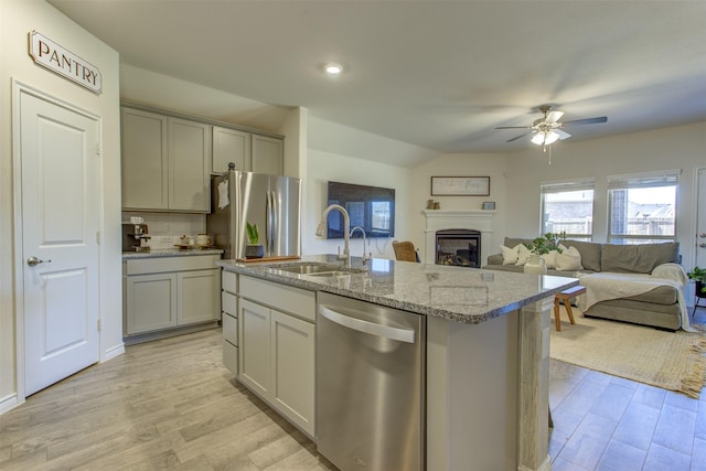 kitchen featuring stainless steel appliances, gray cabinetry, a sink, light stone countertops, and light wood-type flooring