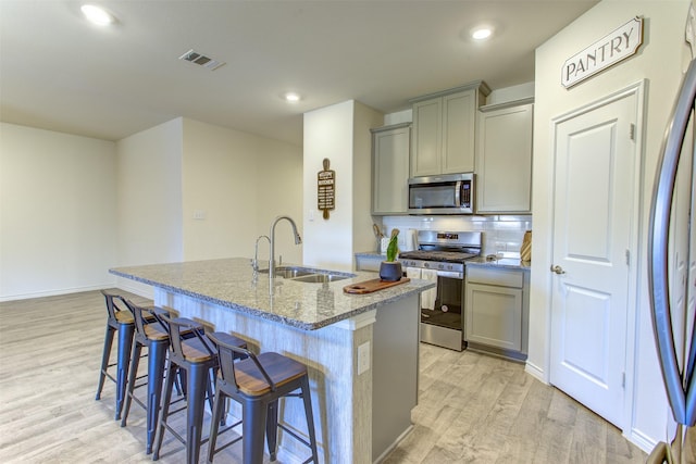 kitchen featuring appliances with stainless steel finishes, a sink, light stone counters, and gray cabinetry