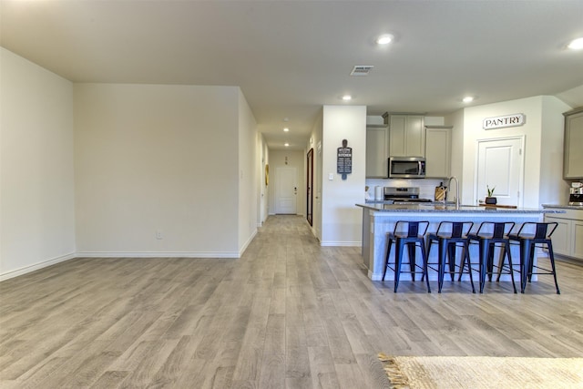 kitchen featuring visible vents, light wood-style flooring, a breakfast bar area, stainless steel appliances, and gray cabinetry