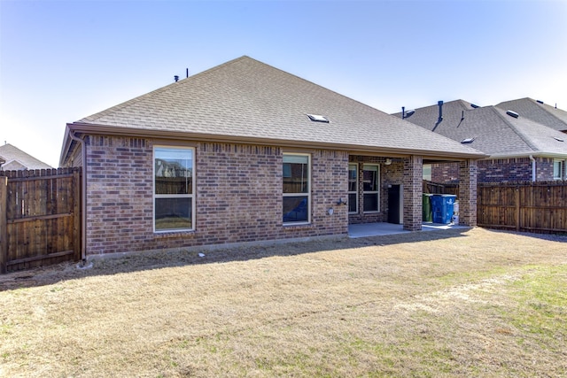 back of property featuring a shingled roof, brick siding, a lawn, and a fenced backyard