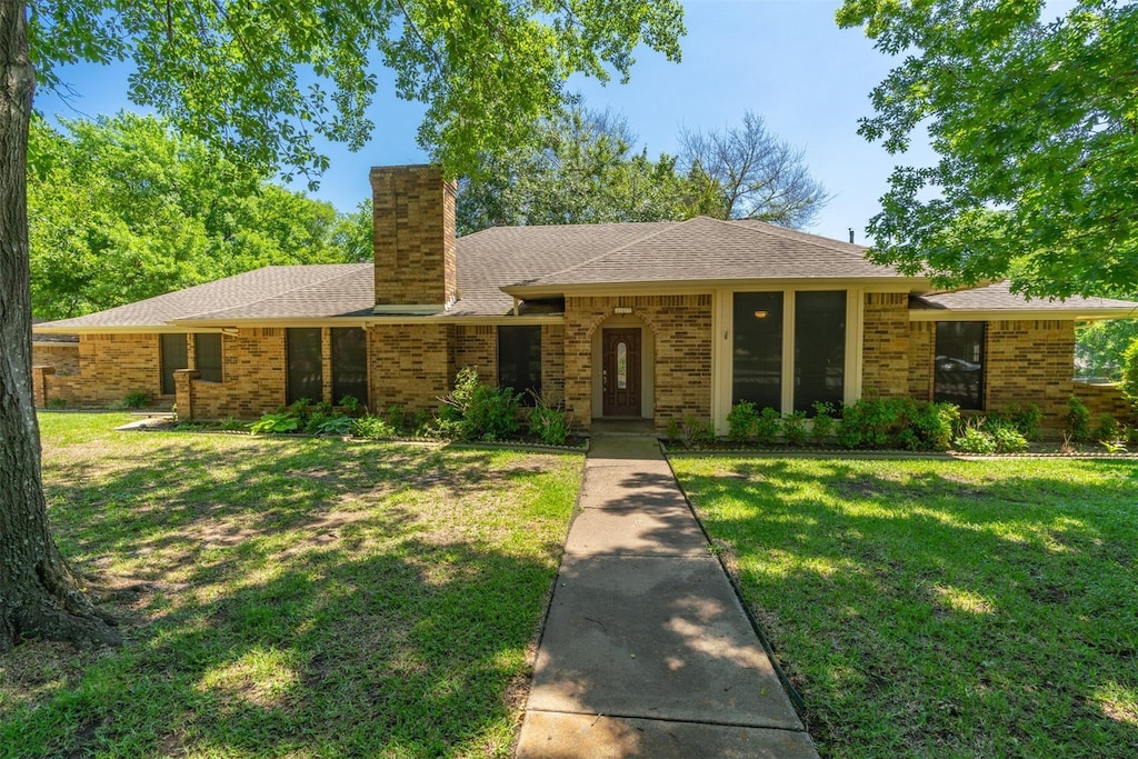 ranch-style house featuring brick siding, a chimney, a front lawn, and roof with shingles