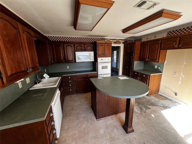 kitchen featuring white appliances, visible vents, a sink, dark countertops, and a center island