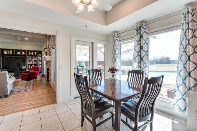 dining room featuring baseboards, ceiling fan, light tile patterned floors, a fireplace, and a raised ceiling