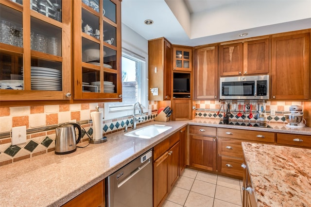 kitchen featuring light stone counters, brown cabinetry, appliances with stainless steel finishes, and a sink