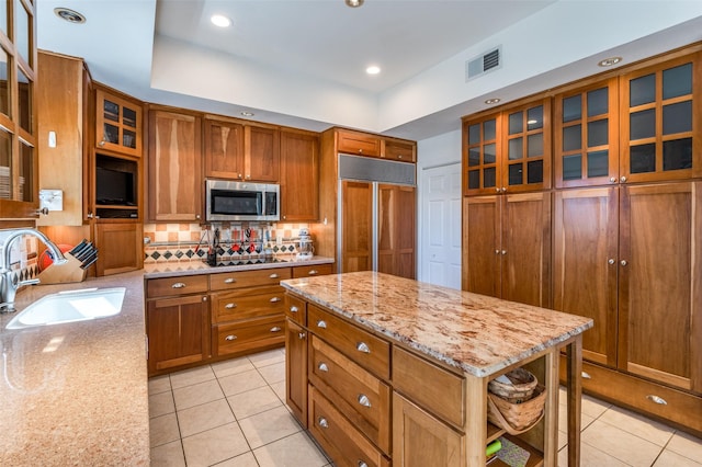 kitchen with a sink, stainless steel microwave, paneled built in refrigerator, and brown cabinetry